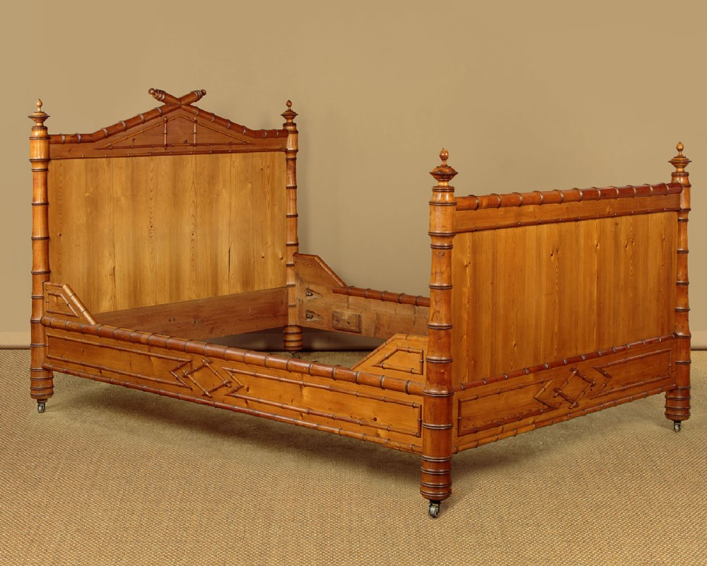 An antique wooden bed frame featuring carved faux bamboo turnings, a raised headboard pediment, decorative lattice side rails, and brass castors.