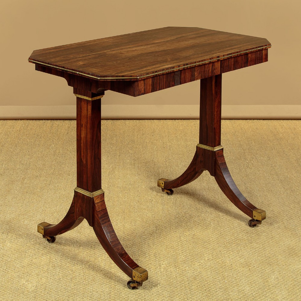 A Regency period rosewood writing table featuring a rectangular top with canted corners, brass beaded trim, twin end supports, and splayed legs with brass castors. View III