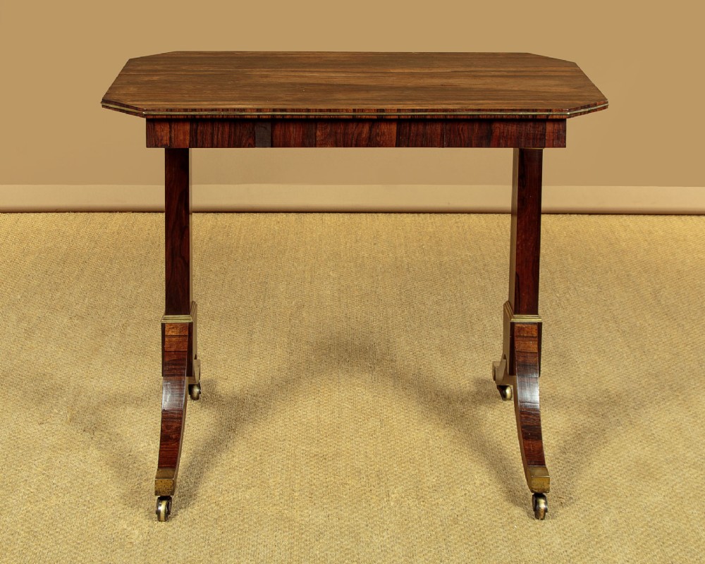 A Regency period rosewood writing table featuring a rectangular top with canted corners, brass beaded trim, twin end supports, and splayed legs with brass castors. View IV