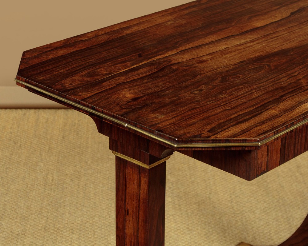 A Regency period rosewood writing table featuring a rectangular top with canted corners, brass beaded trim, twin end supports, and splayed legs with brass castors. View VI
