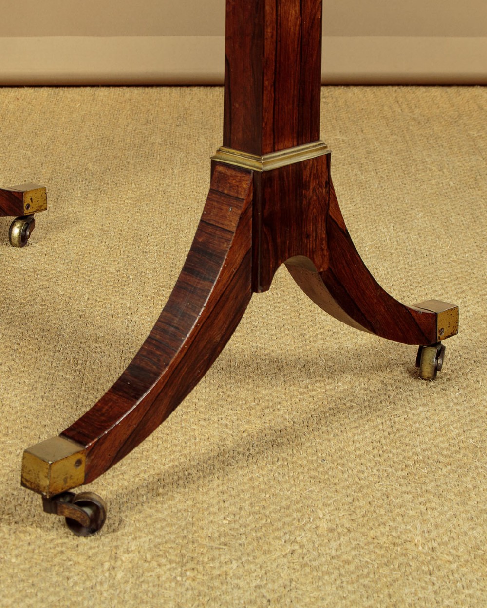 A Regency period rosewood writing table featuring a rectangular top with canted corners, brass beaded trim, twin end supports, and splayed legs with brass castors. View VII