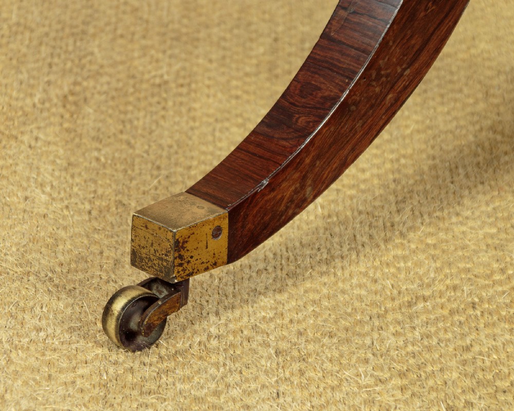 A Regency period rosewood writing table featuring a rectangular top with canted corners, brass beaded trim, twin end supports, and splayed legs with brass castors. View VIII