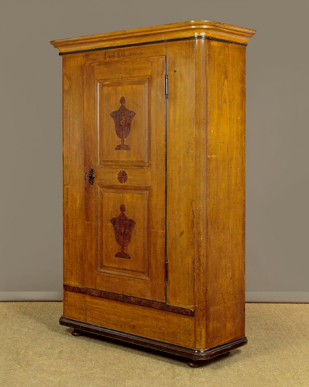 A single-door pine wardrobe featuring hand-painted urn motifs on two panelled sections and a dated inscription near the moulded cornice. View II