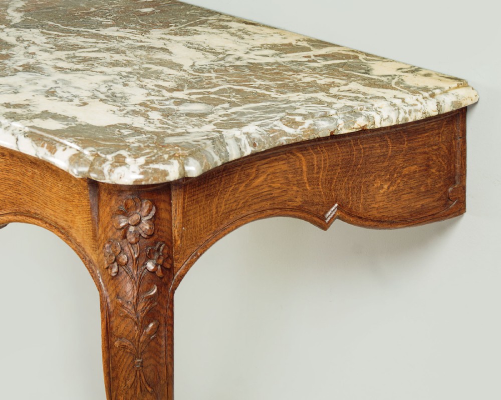 An oak console table featuring a shaped grey marble top, floral relief carvings along the apron, exaggerated cabriole legs, and a scrolled stretcher. View VII