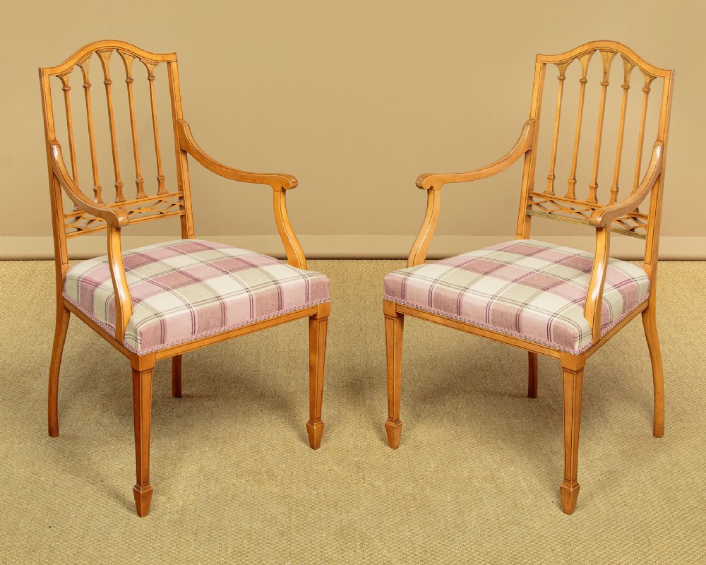 A pair of inlaid satinwood armchairs featuring arched spindle backrests and pink plaid upholstered seats.