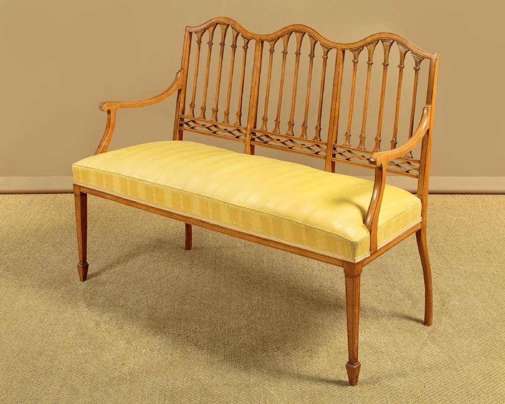 An antique inlaid satinwood triple chair-back settee featuring vertical splats, sweeping arms, and a yellow striped upholstered seat. View III