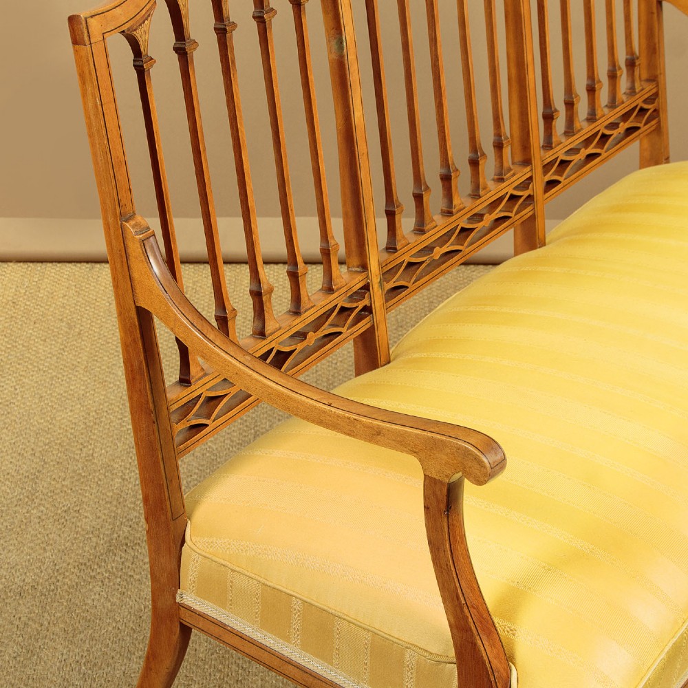 An antique inlaid satinwood triple chair-back settee featuring vertical splats, sweeping arms, and a yellow striped upholstered seat. View VI