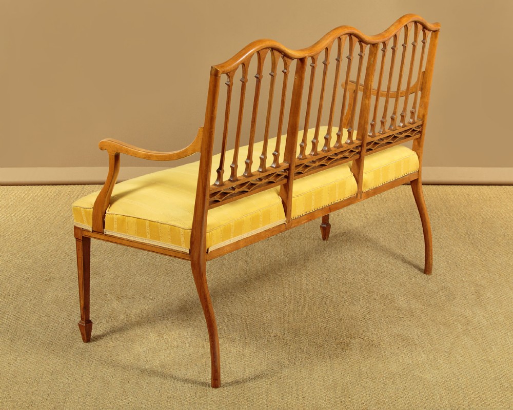 An antique inlaid satinwood triple chair-back settee featuring vertical splats, sweeping arms, and a yellow striped upholstered seat. View XII