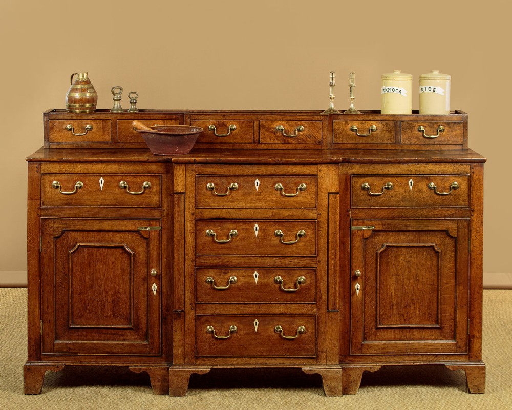 A late 18th-century warm brown oak Welsh dresser base featuring elevated top spice drawers, brass swan-neck handles, central drawers, and side cupboard doors. View II