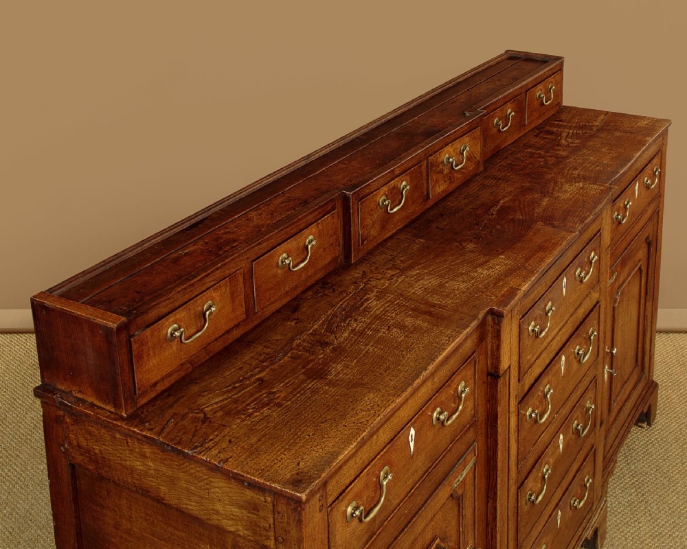 A late 18th-century warm brown oak Welsh dresser base featuring elevated top spice drawers, brass swan-neck handles, central drawers, and side cupboard doors. View VI