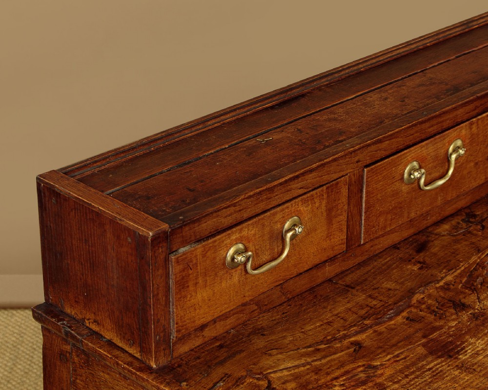 A late 18th-century warm brown oak Welsh dresser base featuring elevated top spice drawers, brass swan-neck handles, central drawers, and side cupboard doors. View VII