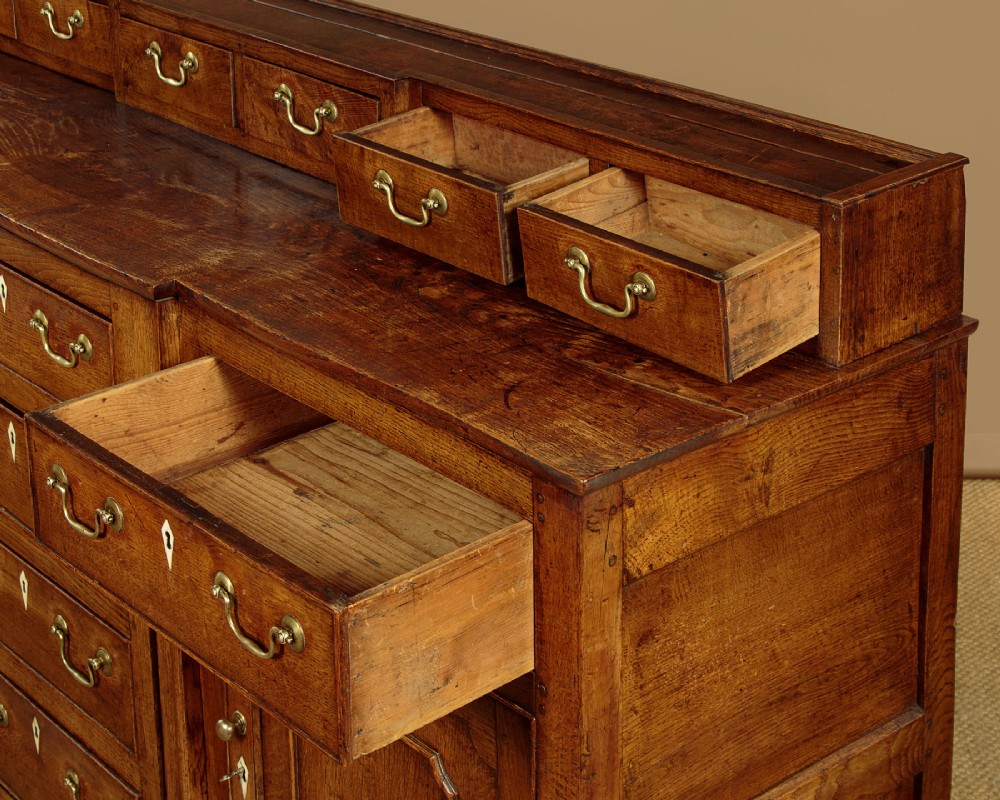 A late 18th-century warm brown oak Welsh dresser base featuring elevated top spice drawers, brass swan-neck handles, central drawers, and side cupboard doors. View VIII