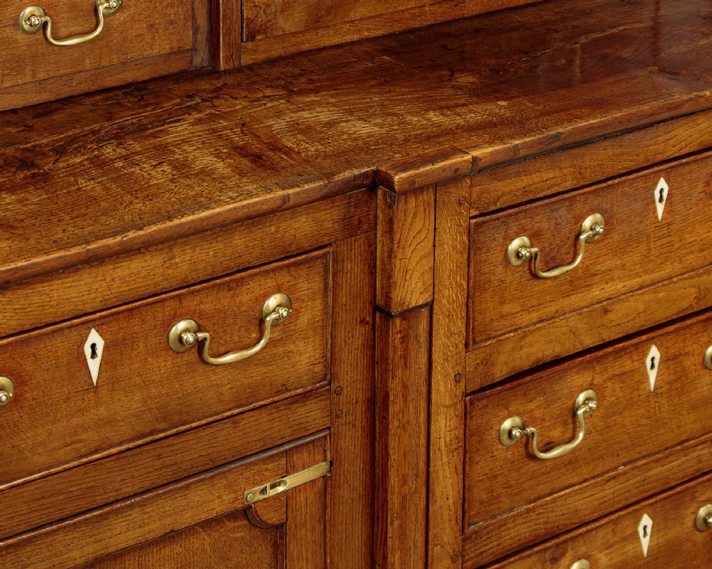 A late 18th-century warm brown oak Welsh dresser base featuring elevated top spice drawers, brass swan-neck handles, central drawers, and side cupboard doors. View IX