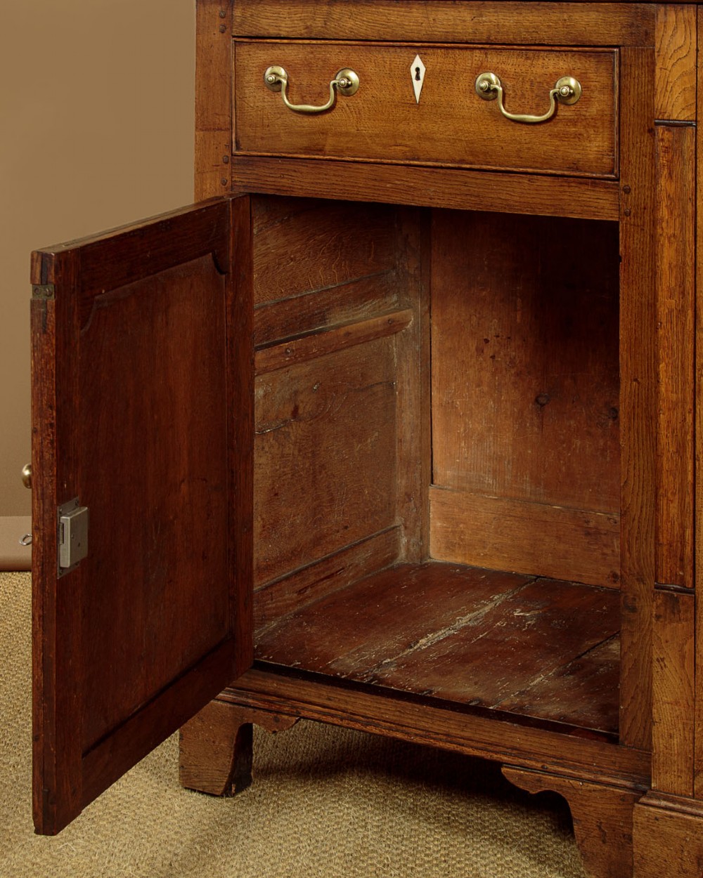 A late 18th-century warm brown oak Welsh dresser base featuring elevated top spice drawers, brass swan-neck handles, central drawers, and side cupboard doors. View XIII
