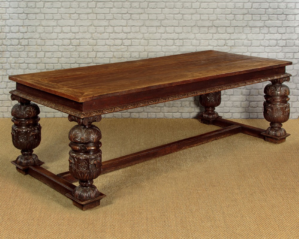A large dark oak refectory dining table featuring heavily carved bulbous turned legs, an ornate frieze, and low stretchers.