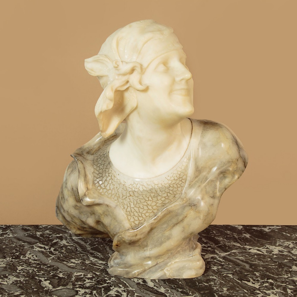 A carved antique alabaster bust of a woman wearing a headscarf tied with a bow, crafted from cream and veined stone.