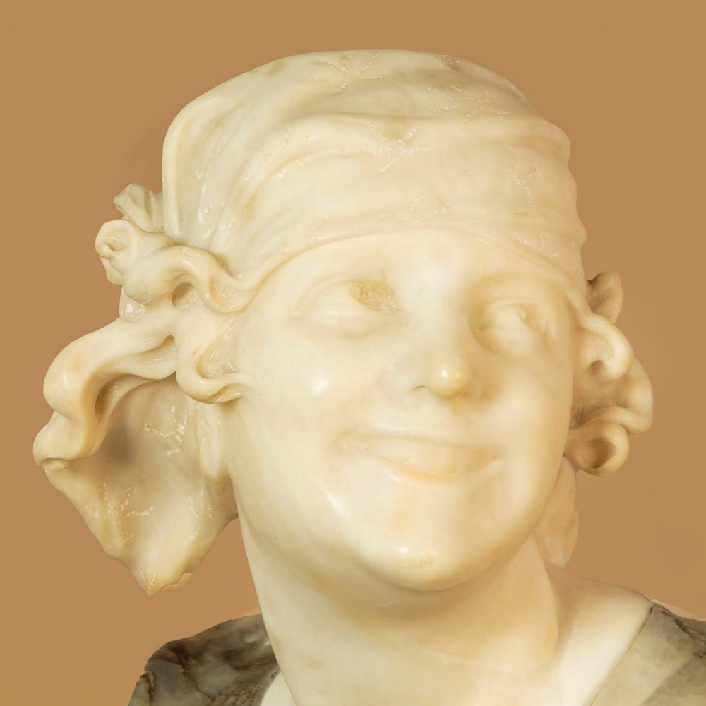 A carved antique alabaster bust of a woman wearing a headscarf tied with a bow, crafted from cream and veined stone. View V