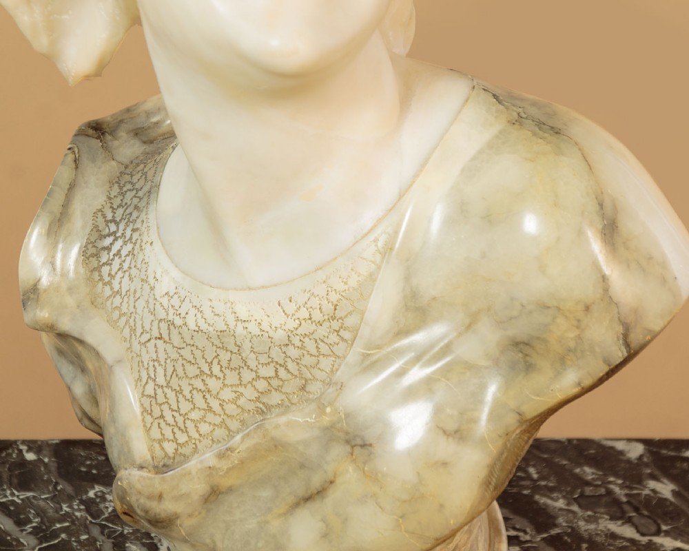 A carved antique alabaster bust of a woman wearing a headscarf tied with a bow, crafted from cream and veined stone. View VI