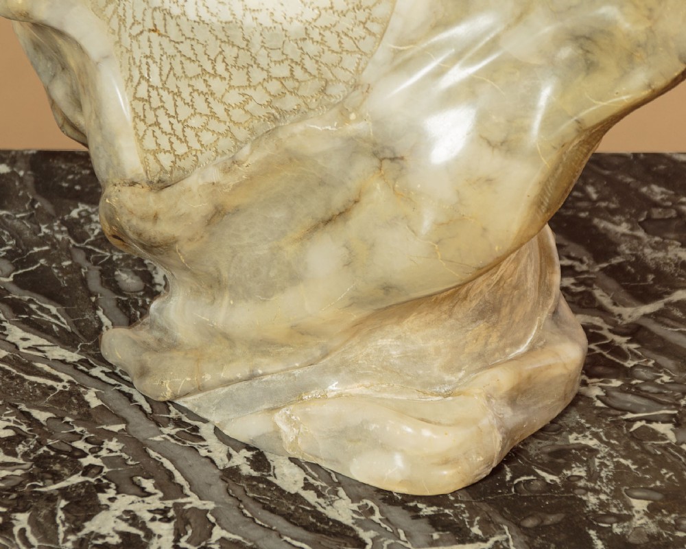 A carved antique alabaster bust of a woman wearing a headscarf tied with a bow, crafted from cream and veined stone. View VIII