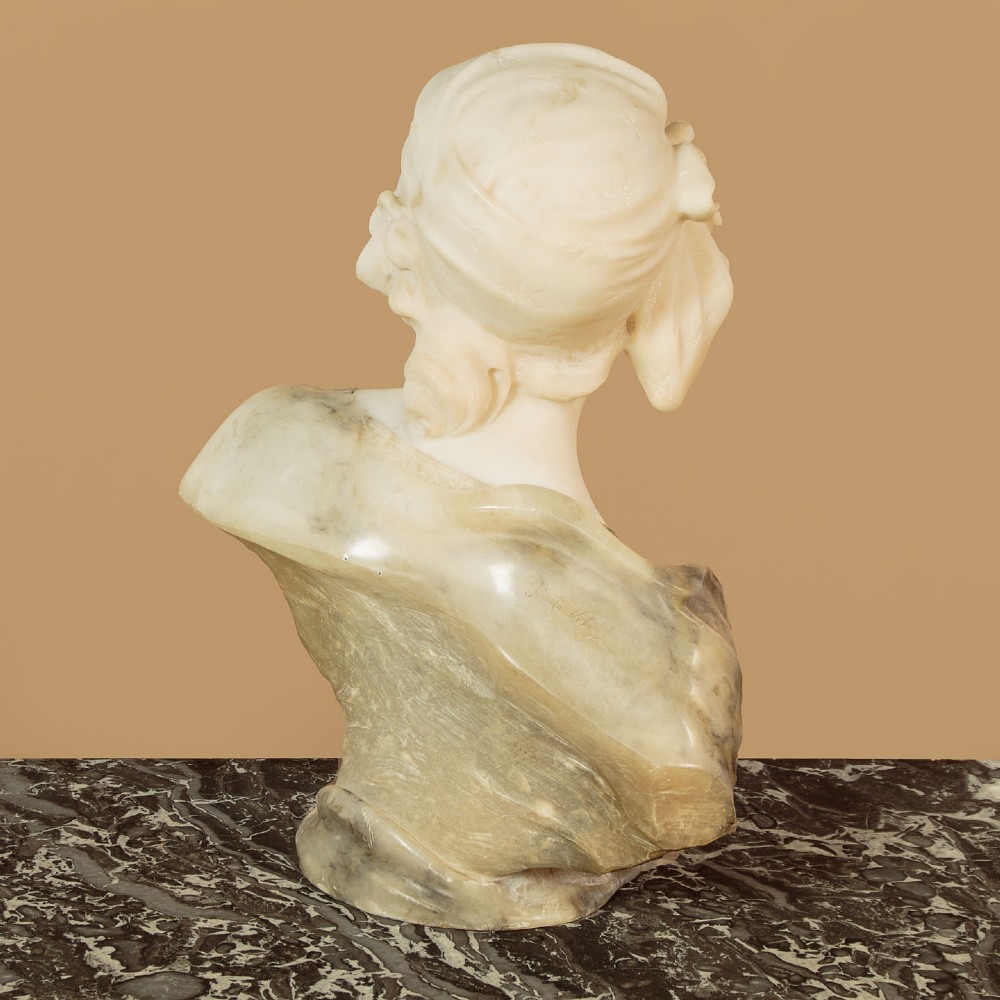 A carved antique alabaster bust of a woman wearing a headscarf tied with a bow, crafted from cream and veined stone. View IX