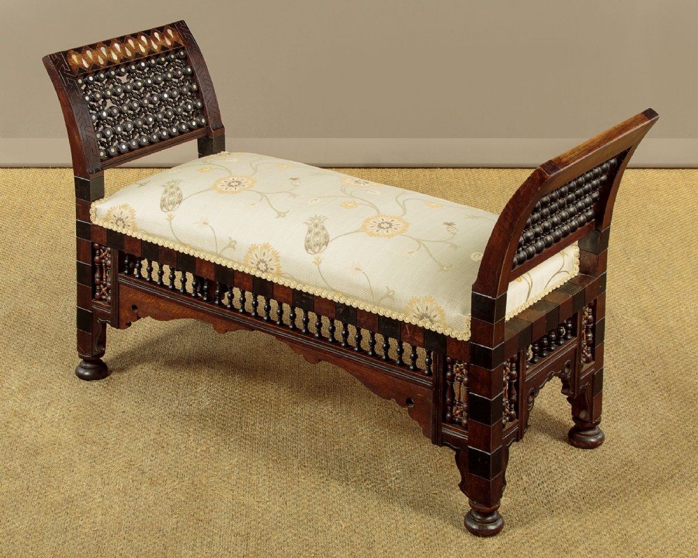A Syrian dark wood window seat c.1920 with mother-of-pearl geometric inlay, turned lattice side panels, and a cream pattern-upholstered cushion.