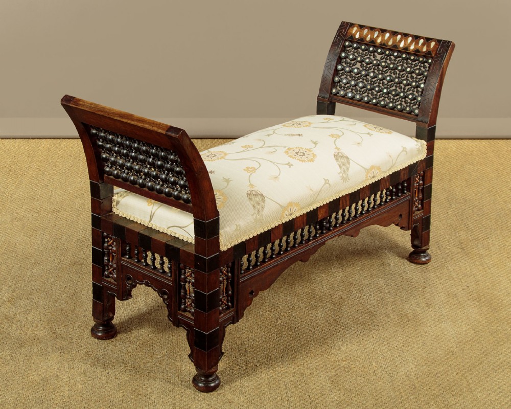 A Syrian dark wood window seat c.1920 with mother-of-pearl geometric inlay, turned lattice side panels, and a cream pattern-upholstered cushion. View III