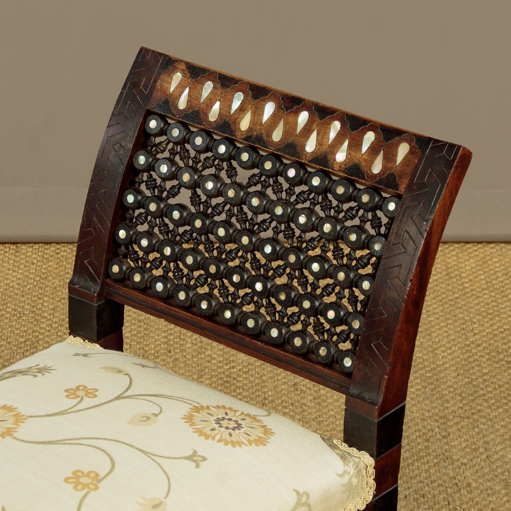 A Syrian dark wood window seat c.1920 with mother-of-pearl geometric inlay, turned lattice side panels, and a cream pattern-upholstered cushion. View IV