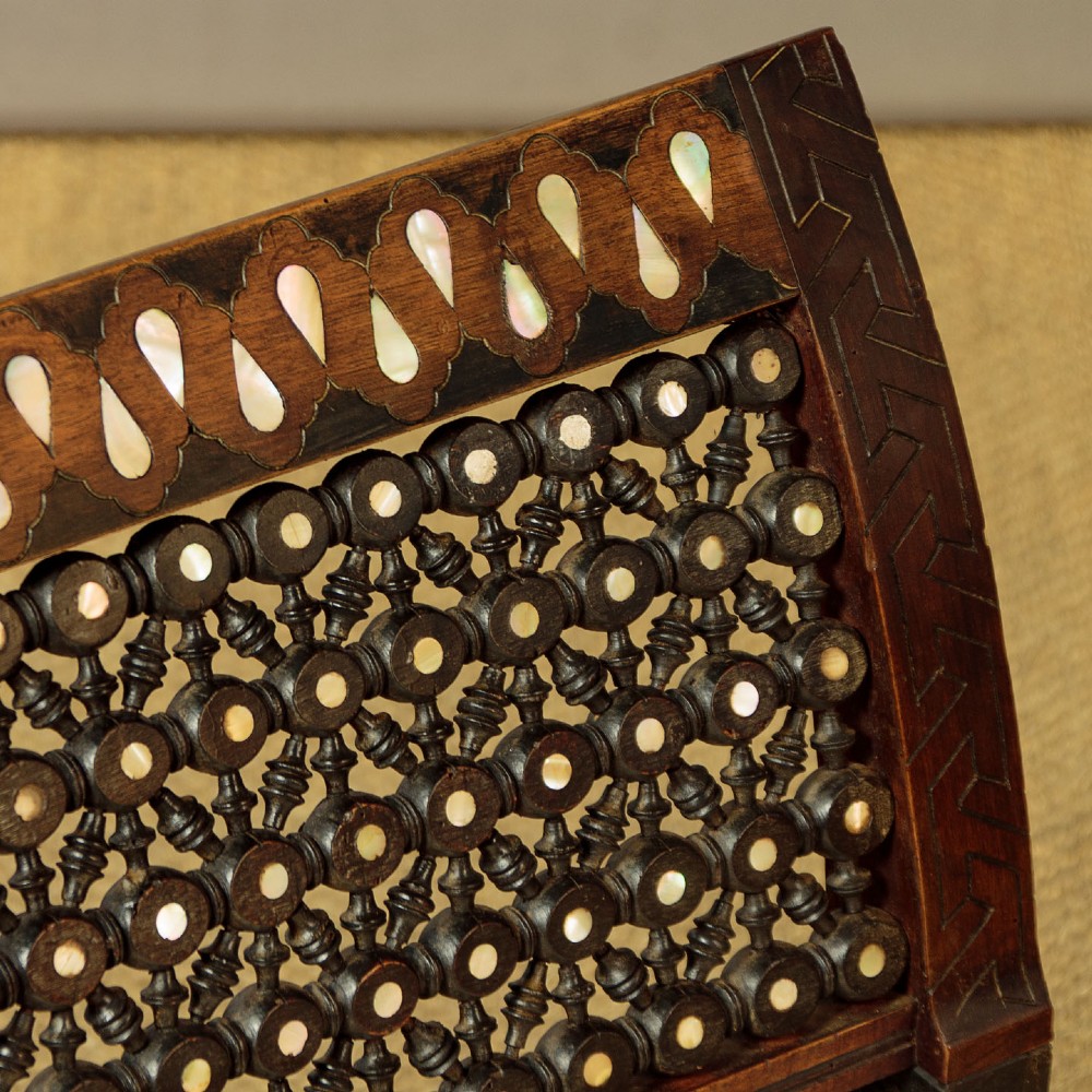 A Syrian dark wood window seat c.1920 with mother-of-pearl geometric inlay, turned lattice side panels, and a cream pattern-upholstered cushion. View V