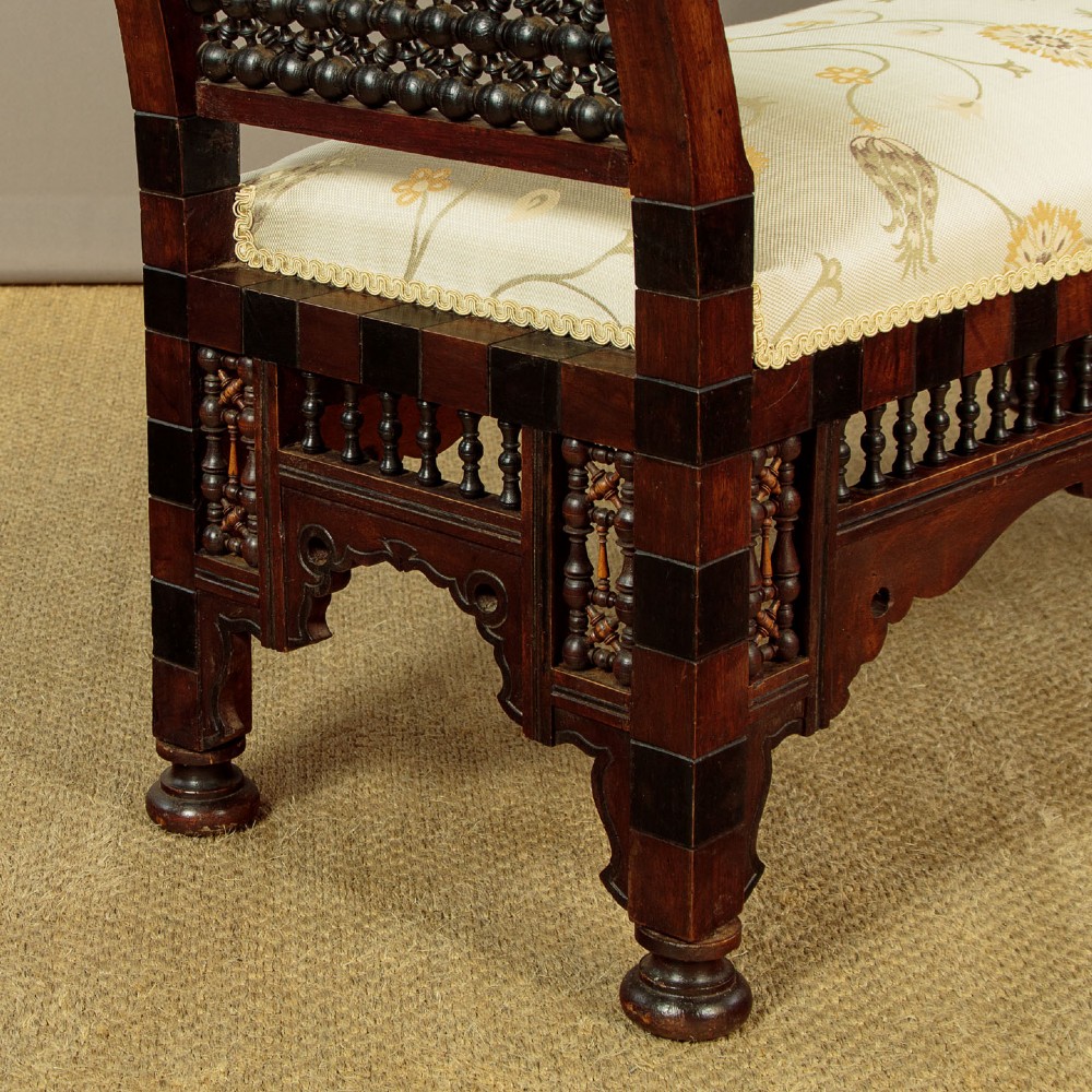 A Syrian dark wood window seat c.1920 with mother-of-pearl geometric inlay, turned lattice side panels, and a cream pattern-upholstered cushion. View X