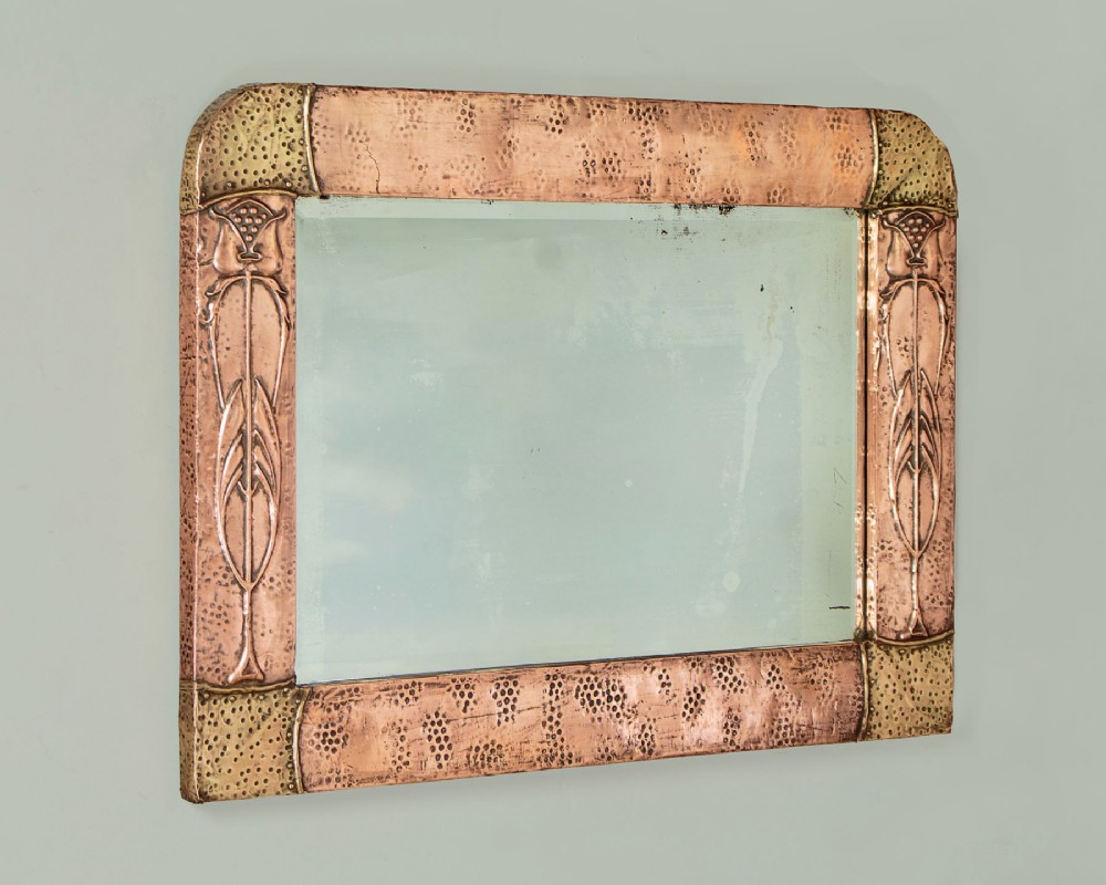 A rectangular Arts and Crafts wall mirror featuring a hand-hammered copper frame accented with repousse floral motifs and brass corner spandrels. View II