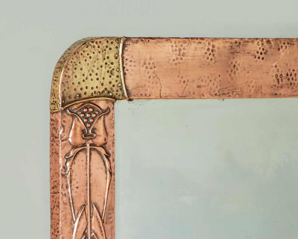 A rectangular Arts and Crafts wall mirror featuring a hand-hammered copper frame accented with repousse floral motifs and brass corner spandrels. View III