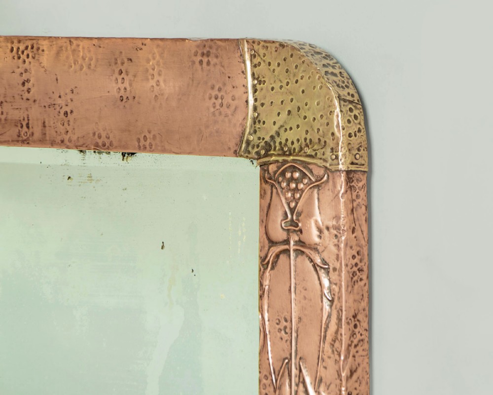 A rectangular Arts and Crafts wall mirror featuring a hand-hammered copper frame accented with repousse floral motifs and brass corner spandrels. View IV