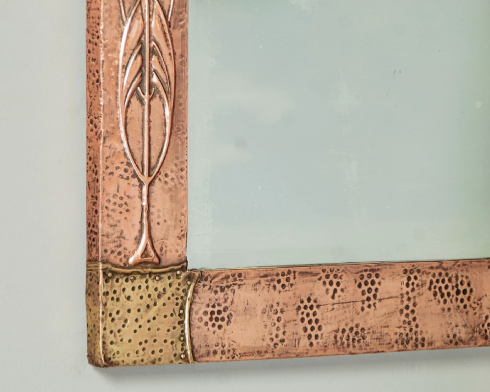 A rectangular Arts and Crafts wall mirror featuring a hand-hammered copper frame accented with repousse floral motifs and brass corner spandrels. View VII