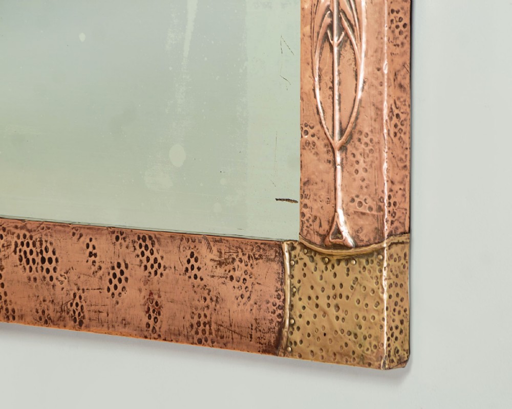 A rectangular Arts and Crafts wall mirror featuring a hand-hammered copper frame accented with repousse floral motifs and brass corner spandrels. View VIII