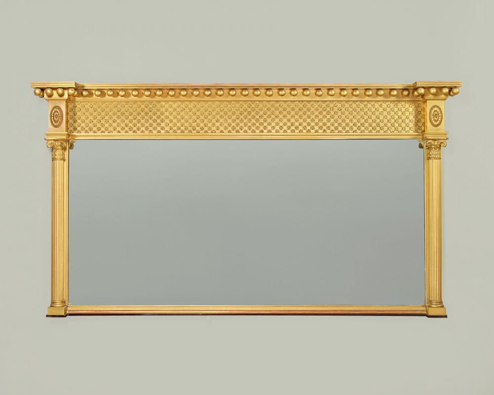 A large rectangular giltwood overmantel mirror featuring a decorated upper frieze with spherical mouldings and fluted side columns.