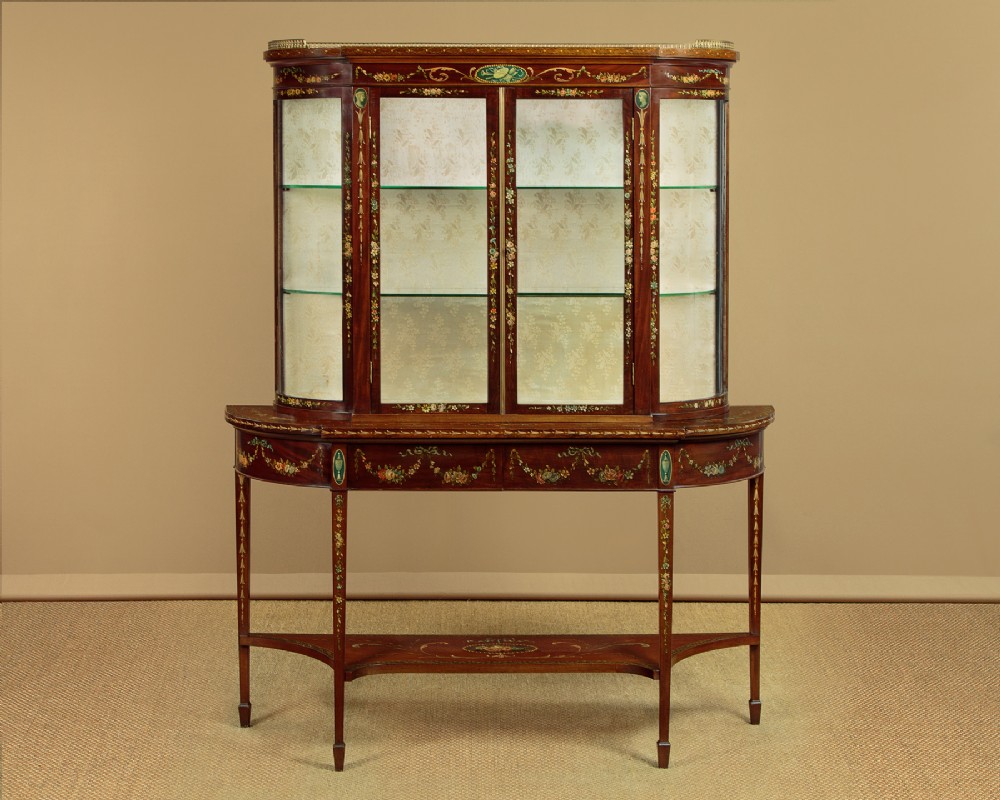 A dark mahogany display cabinet featuring hand-painted floral swags, classical urns, glass side panels, twin glazed doors, and tapered legs with an undertier.