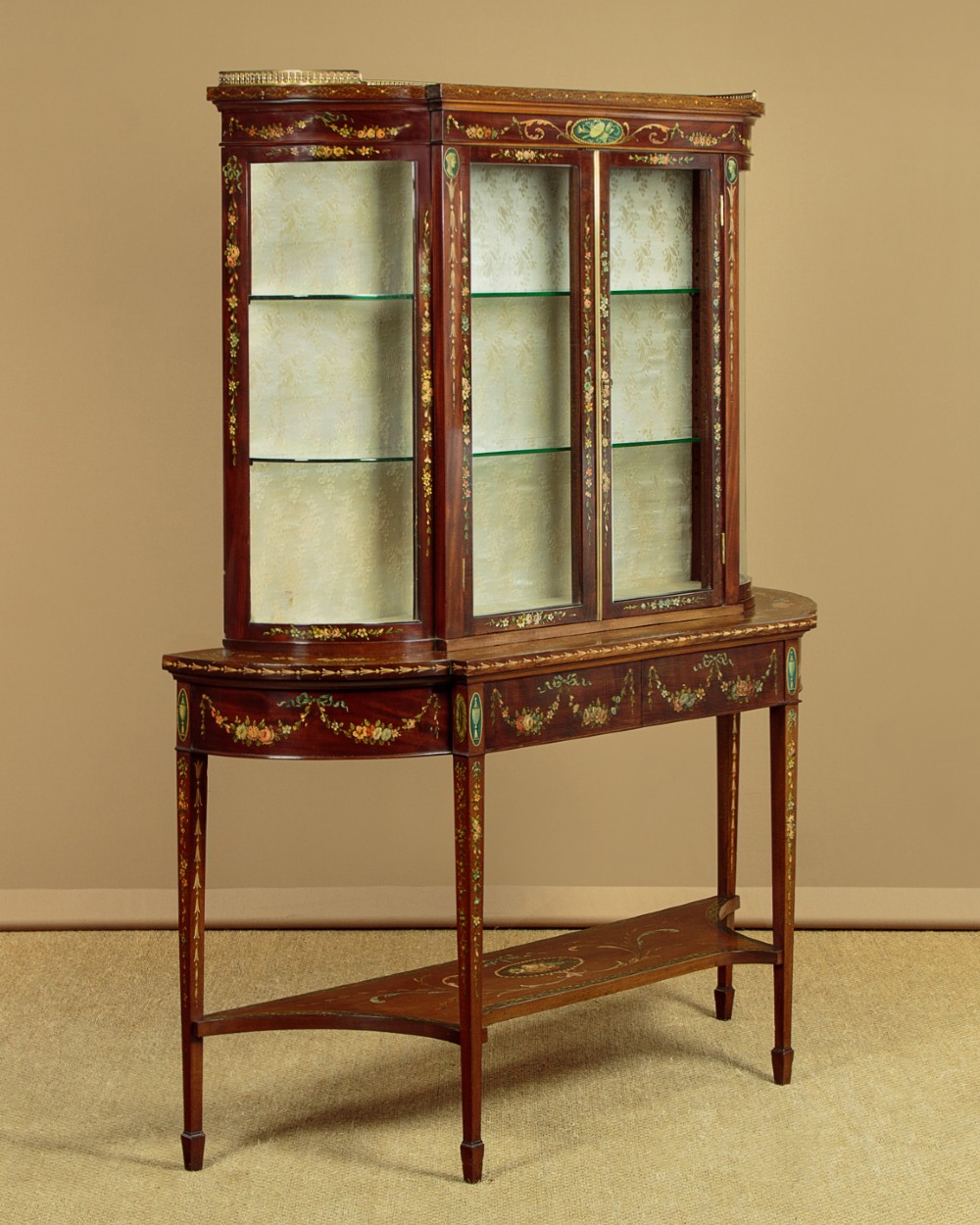 A dark mahogany display cabinet featuring hand-painted floral swags, classical urns, glass side panels, twin glazed doors, and tapered legs with an undertier. View II
