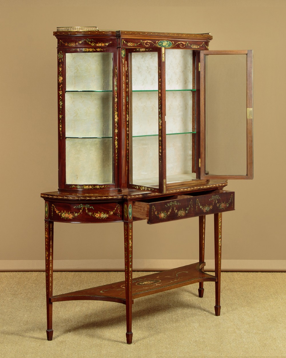 A dark mahogany display cabinet featuring hand-painted floral swags, classical urns, glass side panels, twin glazed doors, and tapered legs with an undertier. View III