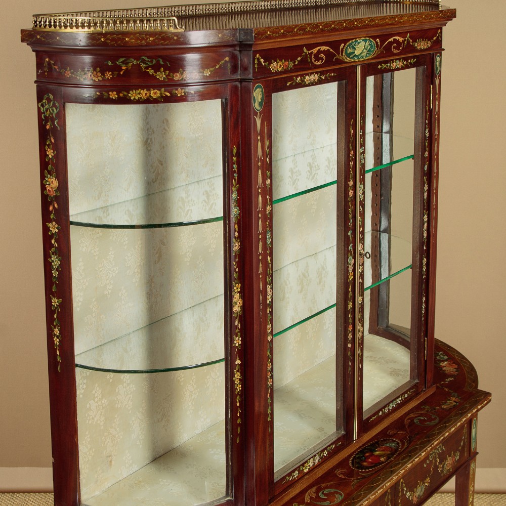 A dark mahogany display cabinet featuring hand-painted floral swags, classical urns, glass side panels, twin glazed doors, and tapered legs with an undertier. View V