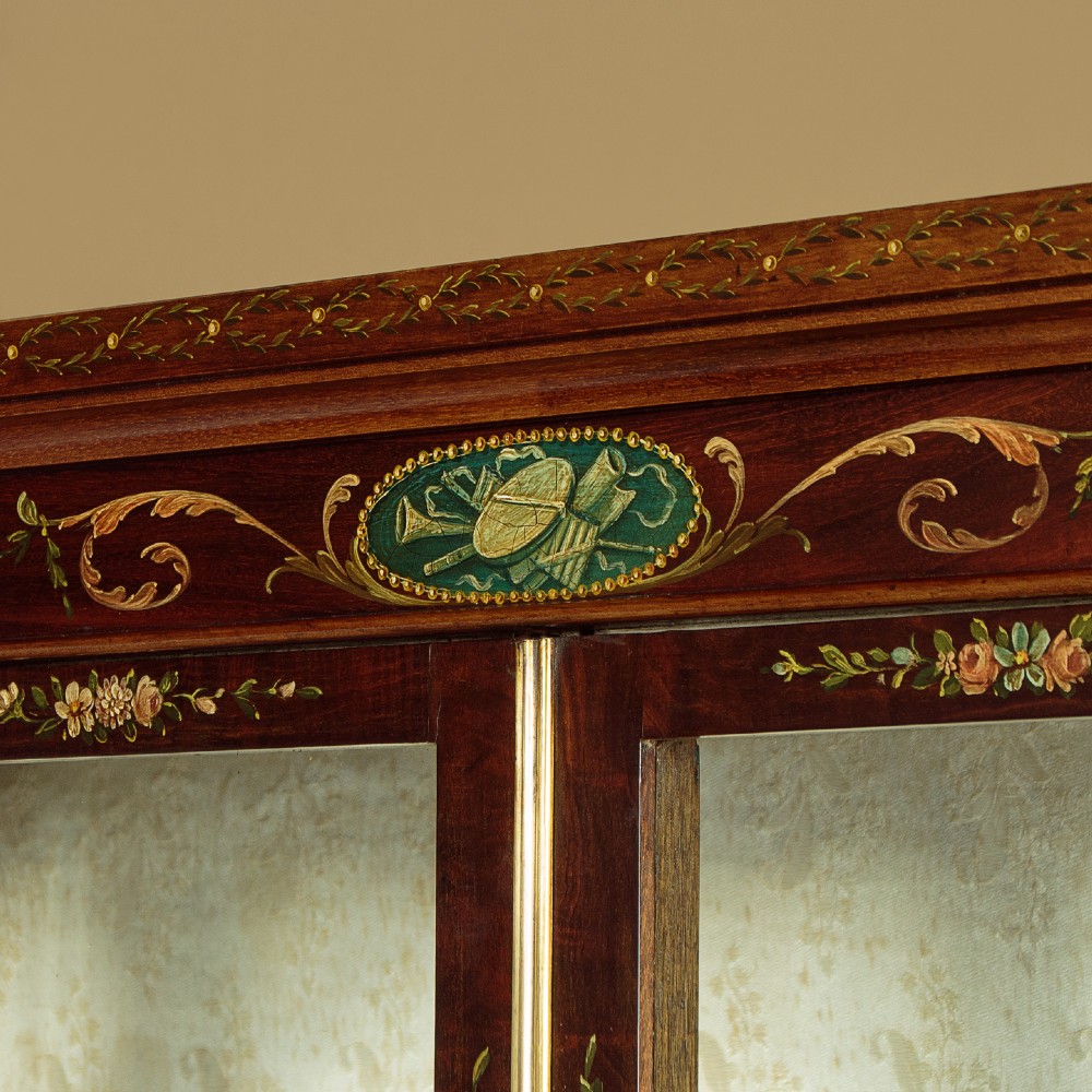 A dark mahogany display cabinet featuring hand-painted floral swags, classical urns, glass side panels, twin glazed doors, and tapered legs with an undertier. View VI