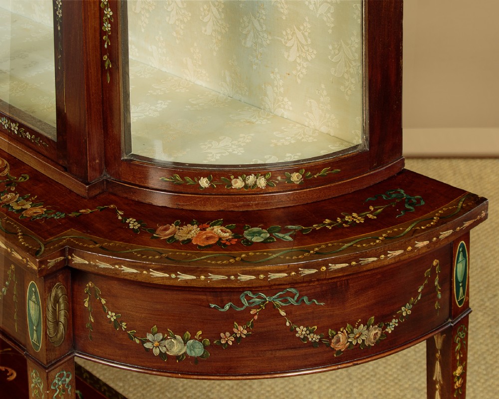 A dark mahogany display cabinet featuring hand-painted floral swags, classical urns, glass side panels, twin glazed doors, and tapered legs with an undertier. View VIII