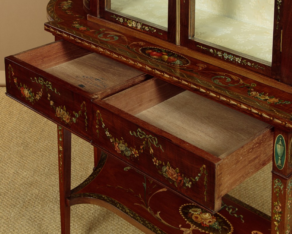 A dark mahogany display cabinet featuring hand-painted floral swags, classical urns, glass side panels, twin glazed doors, and tapered legs with an undertier. View IX