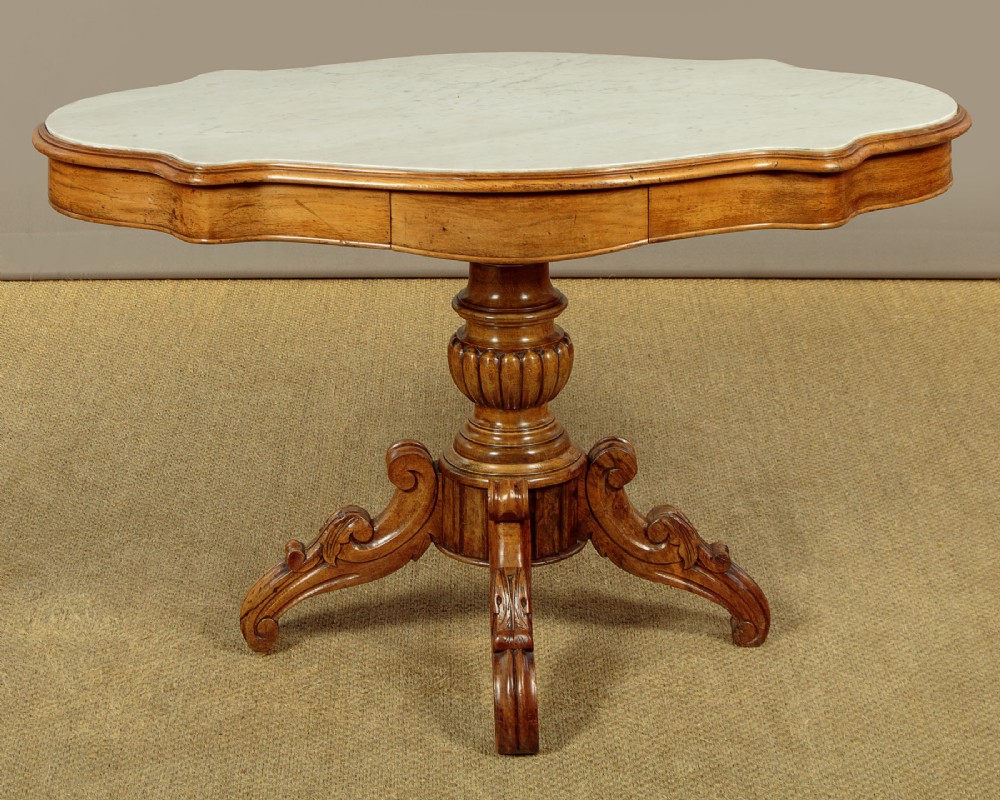 A nineteenth-century Victorian walnut centre table featuring a serpentine white marble top resting on a carved pedestal stem with scrolled tripod legs.
