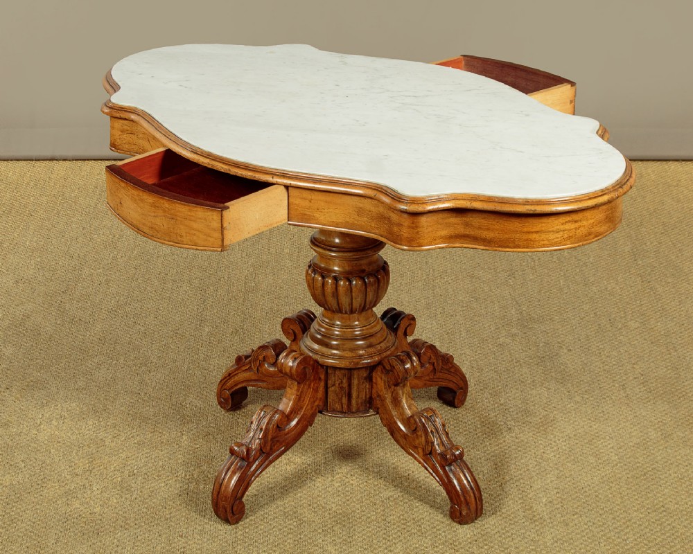 A nineteenth-century Victorian walnut centre table featuring a serpentine white marble top resting on a carved pedestal stem with scrolled tripod legs. View IV