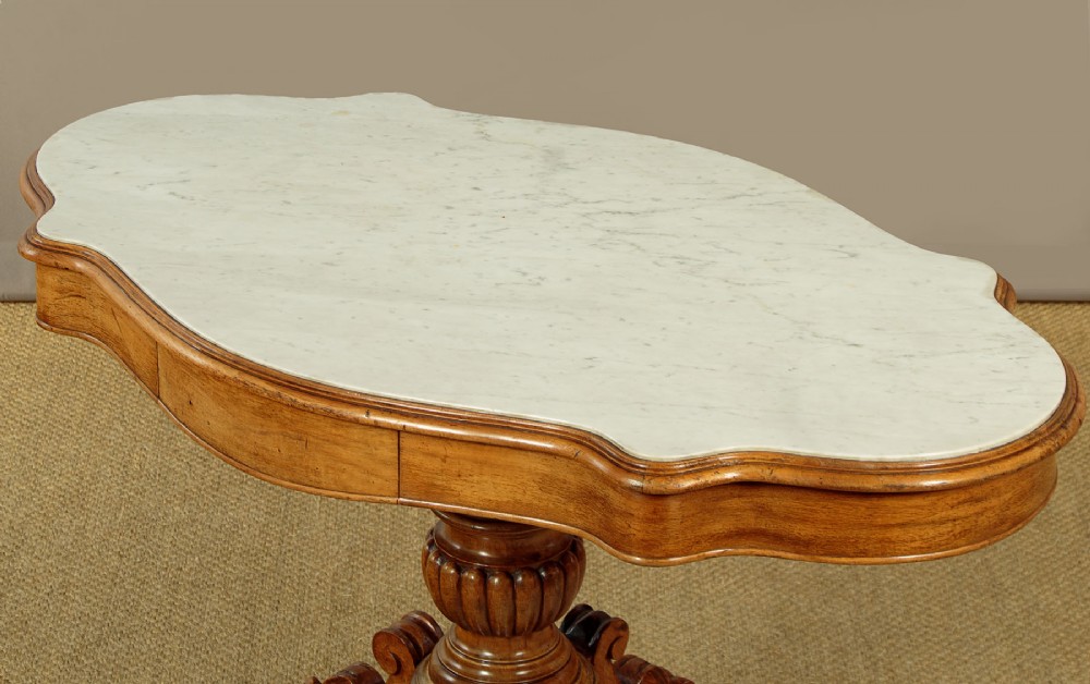A nineteenth-century Victorian walnut centre table featuring a serpentine white marble top resting on a carved pedestal stem with scrolled tripod legs. View V