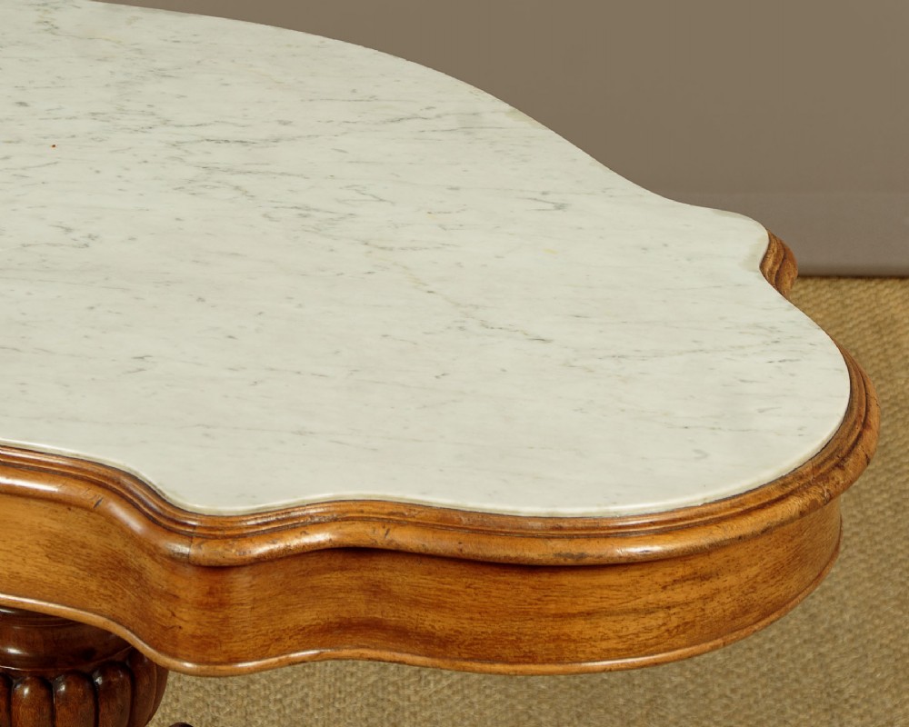 A nineteenth-century Victorian walnut centre table featuring a serpentine white marble top resting on a carved pedestal stem with scrolled tripod legs. View VI