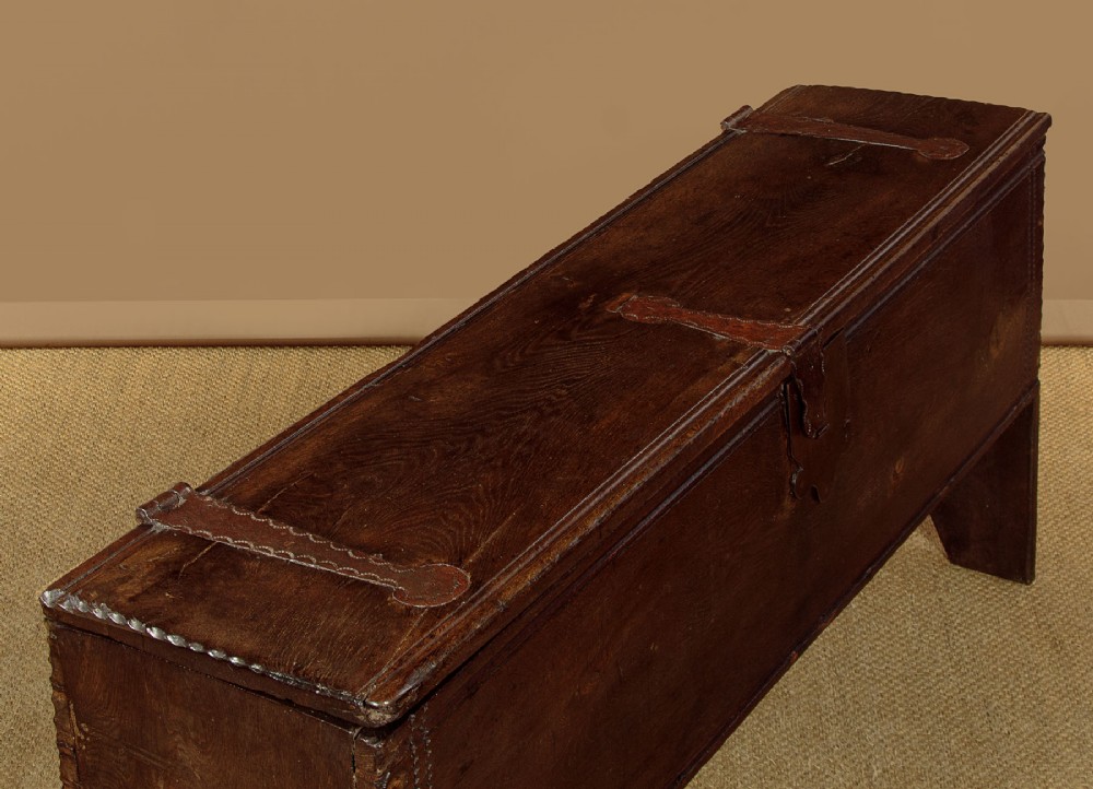 A long dark oak boarded sword chest featuring iron strap hinges and slab end supports. View V
