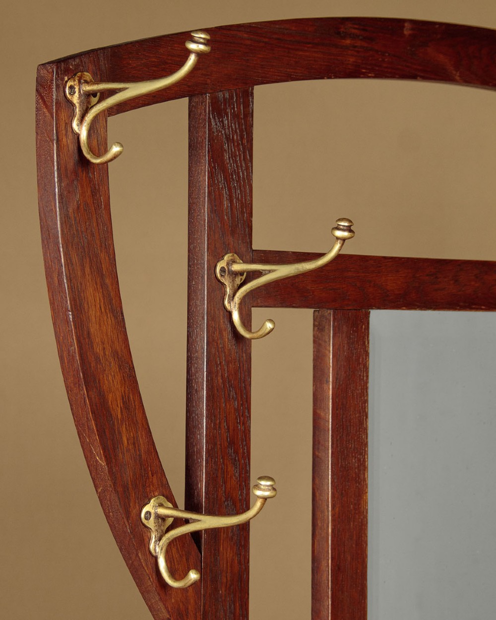 An Art Nouveau oak hallstand featuring an arched upper frame, brass coat hooks, central mirror, glove box, and bottom umbrella stand with two brass drip trays. View IV