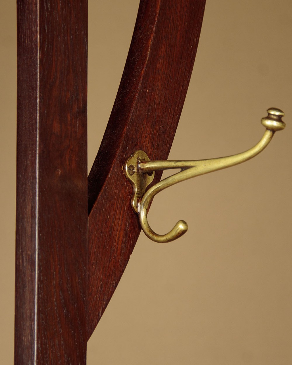 An Art Nouveau oak hallstand featuring an arched upper frame, brass coat hooks, central mirror, glove box, and bottom umbrella stand with two brass drip trays. View V
