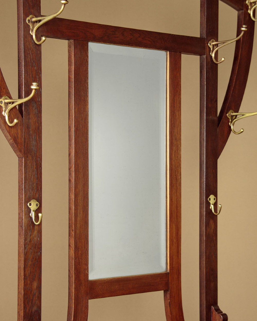 An Art Nouveau oak hallstand featuring an arched upper frame, brass coat hooks, central mirror, glove box, and bottom umbrella stand with two brass drip trays. View VI